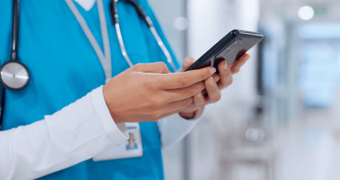 Healthcare professional in blue scrubs using the X.eMAR mobile application to access patient medication records and verify doses.